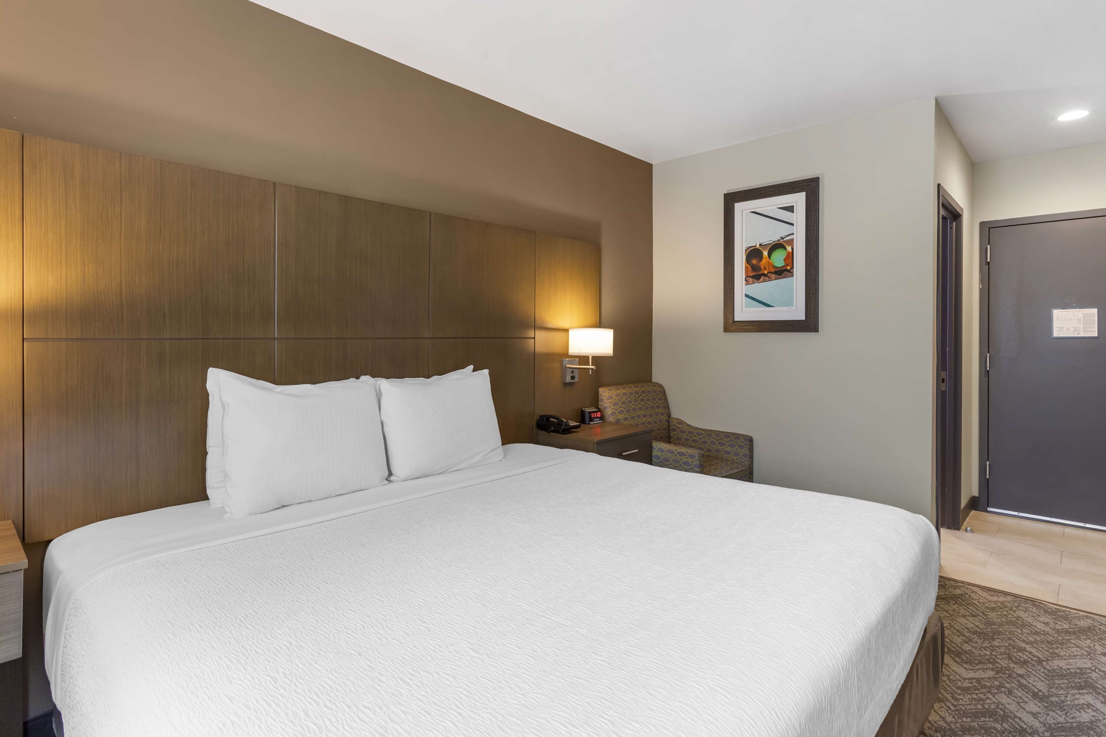 Een hotelkamer met een groot bed, een nachtkastje met een lamp, een stoel en een deur.