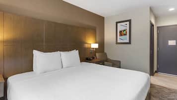 A hotel room with a large bed, a bedside table with a lamp, a chair, and a door.