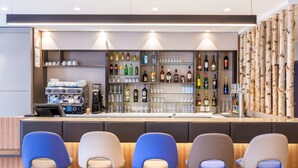 A bar area with a counter, shelves of bottles, glasses, and a coffee machine. There are five chairs in front of the bar. - Best Western Le Beffroi (Loos)