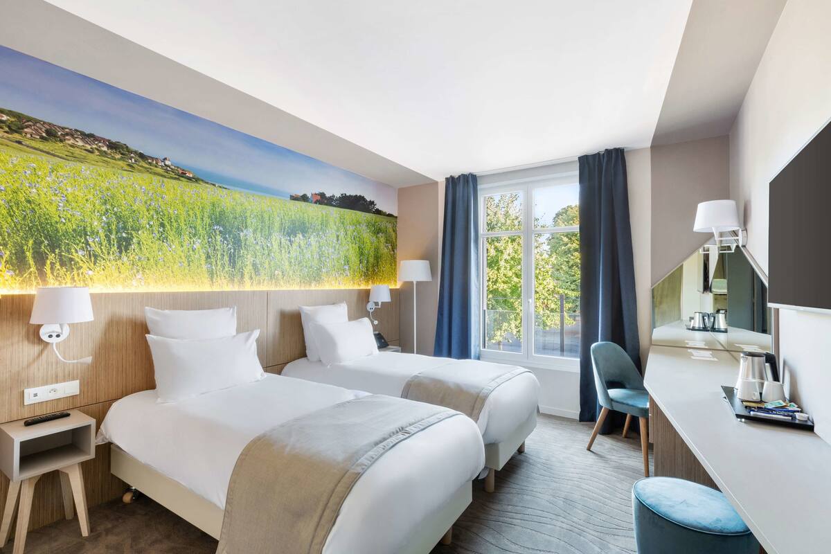 A hotel room with two beds, a desk, and a large window with curtains.