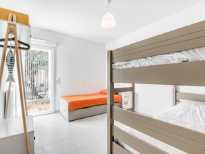 Une chambre avec un lit superposé, un plafond blanc, un luminaire suspendu et une vue sur un balcon avec une chaise blanche.