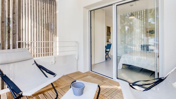 En moderne balkon med trægulv, to hvide loungesenge og en glasdør til et tilstødende rum.