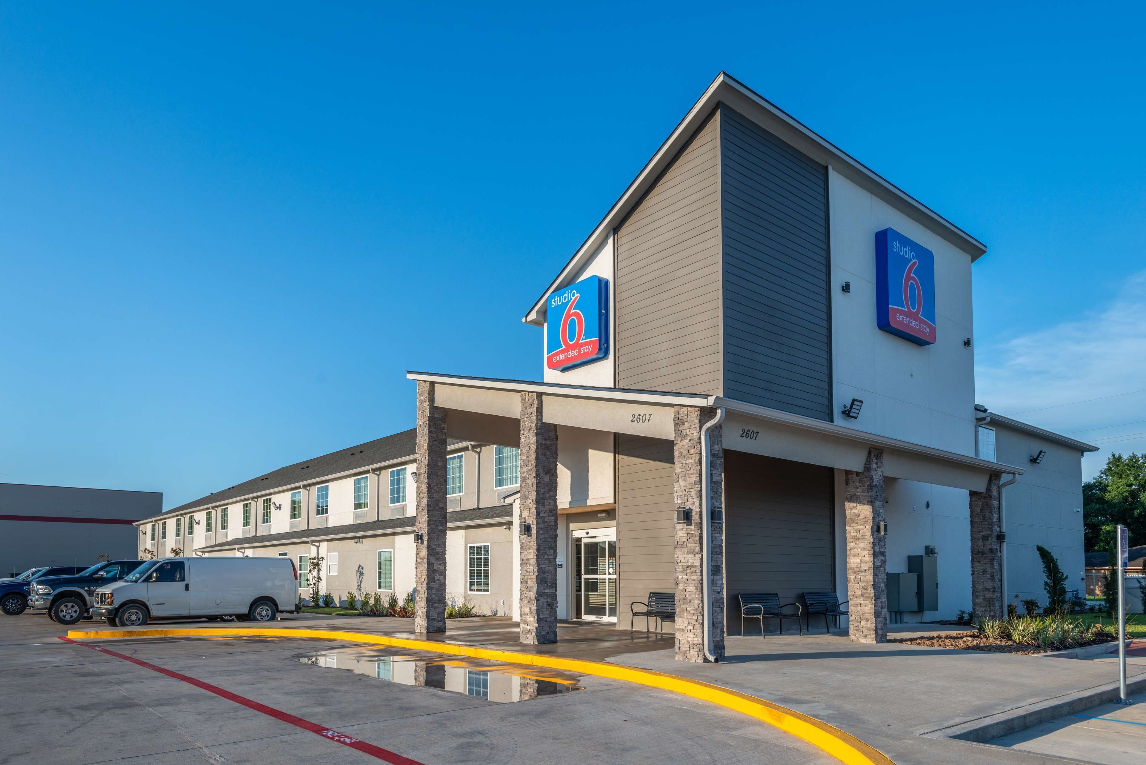 A modern hotel with a prominent 'Studio 6' sign, a covered entrance, and a parking lot with a white van.