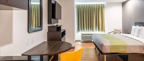 A modern hotel room with a bed, a desk, a chair, a TV, and a window with curtains.