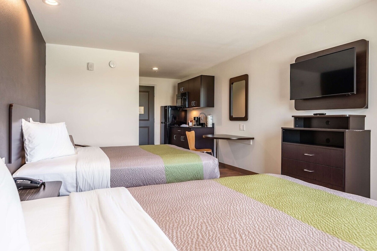 A hotel room with two beds, a TV, a desk, and a mirror.
