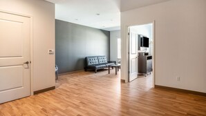 A spacious living area with a wooden floor, a grey sofa, and a television in the background. - Studio 6 Lake Charles, LA (Lake Charles)