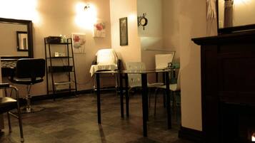 A room with a fireplace, a desk with a chair, a small table with chairs, and a mirror on the wall.