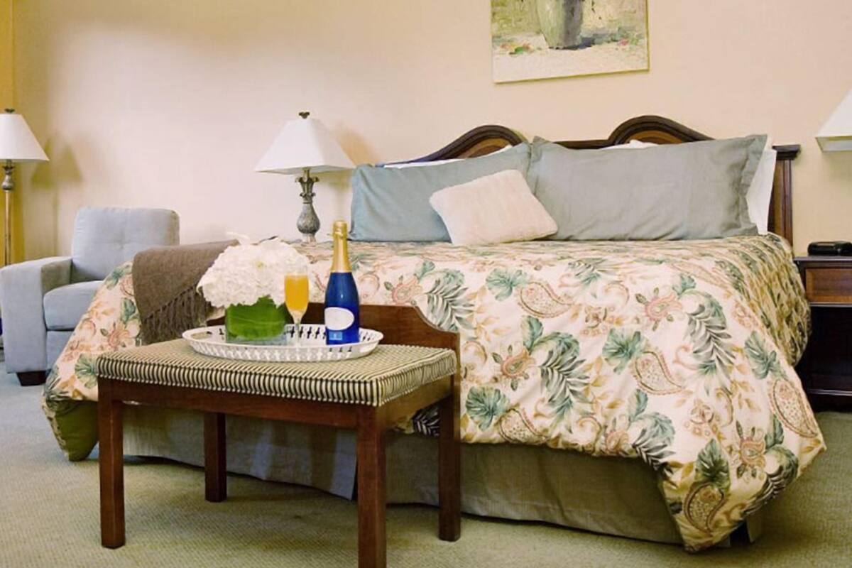 A hotel room with a bed, bedside lamps, a chair, a tray with flowers and champagne, and a painting on the wall.