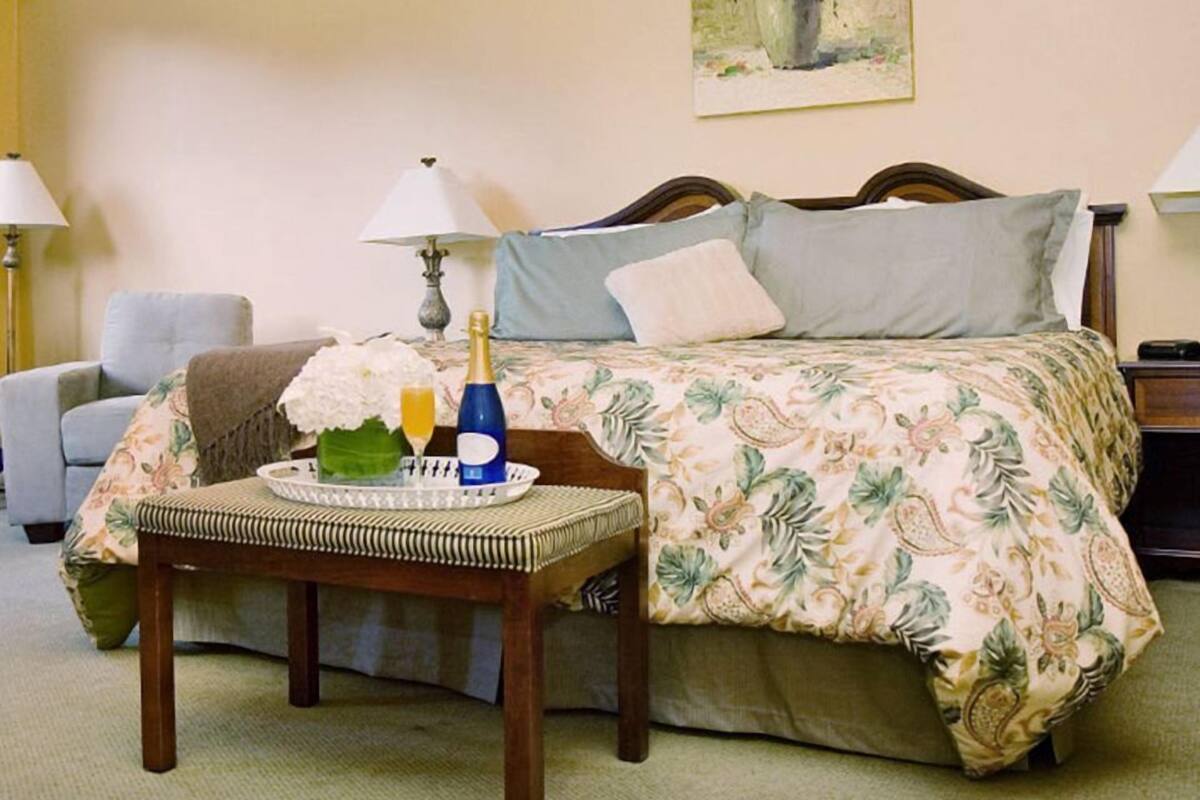 A neatly arranged bedroom with a bed, bedside lamps, a chair, and a tray with a bottle and flowers.