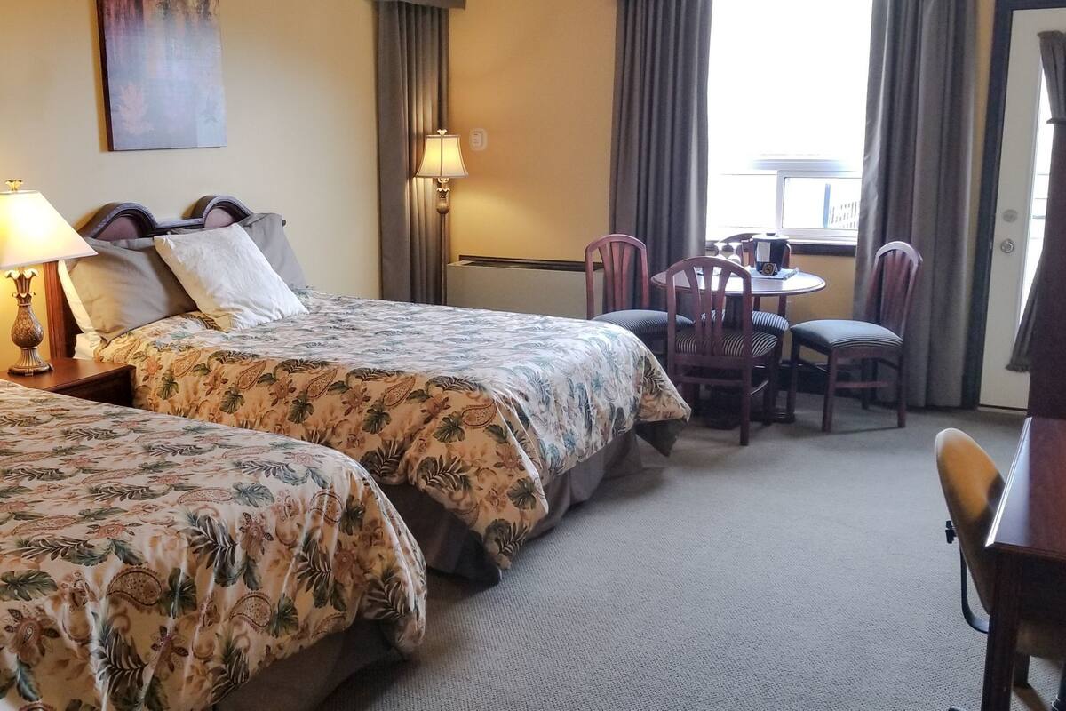 A hotel room with two beds, a desk, chairs, and a window with curtains.