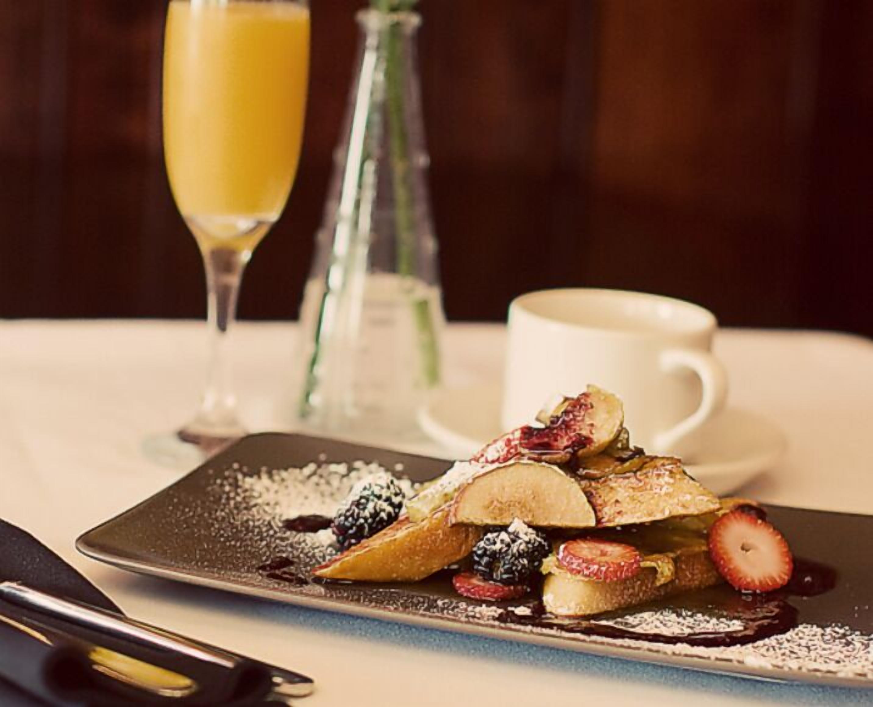 A breakfast plate with pancakes, berries, and powdered sugar, a glass of orange juice, and a cup of coffee on a table.