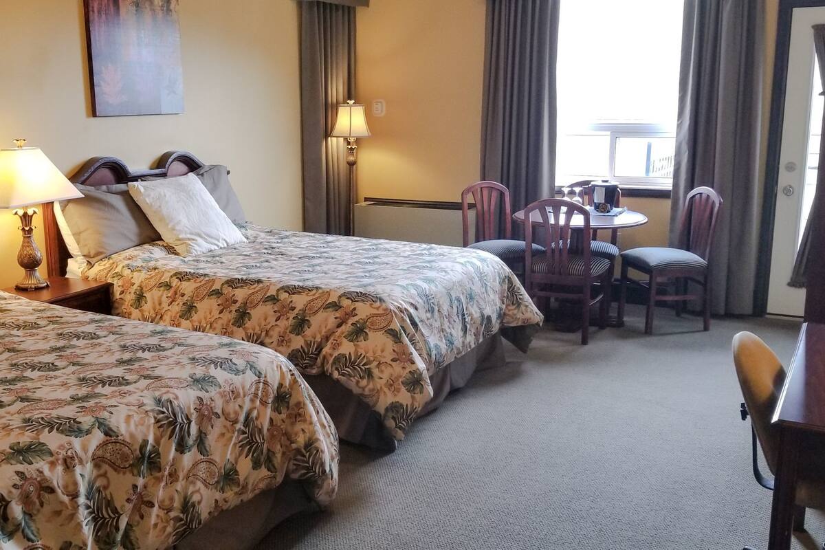 A hotel room with two beds, a desk, and a chair.