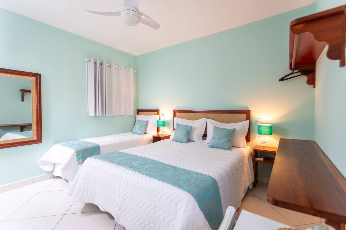 Ein Hotelzimmer mit zwei Betten, einem Deckenventilator, einem Nachttisch aus Holz mit Lampen, einem Spiegel und einer Holzkommode.