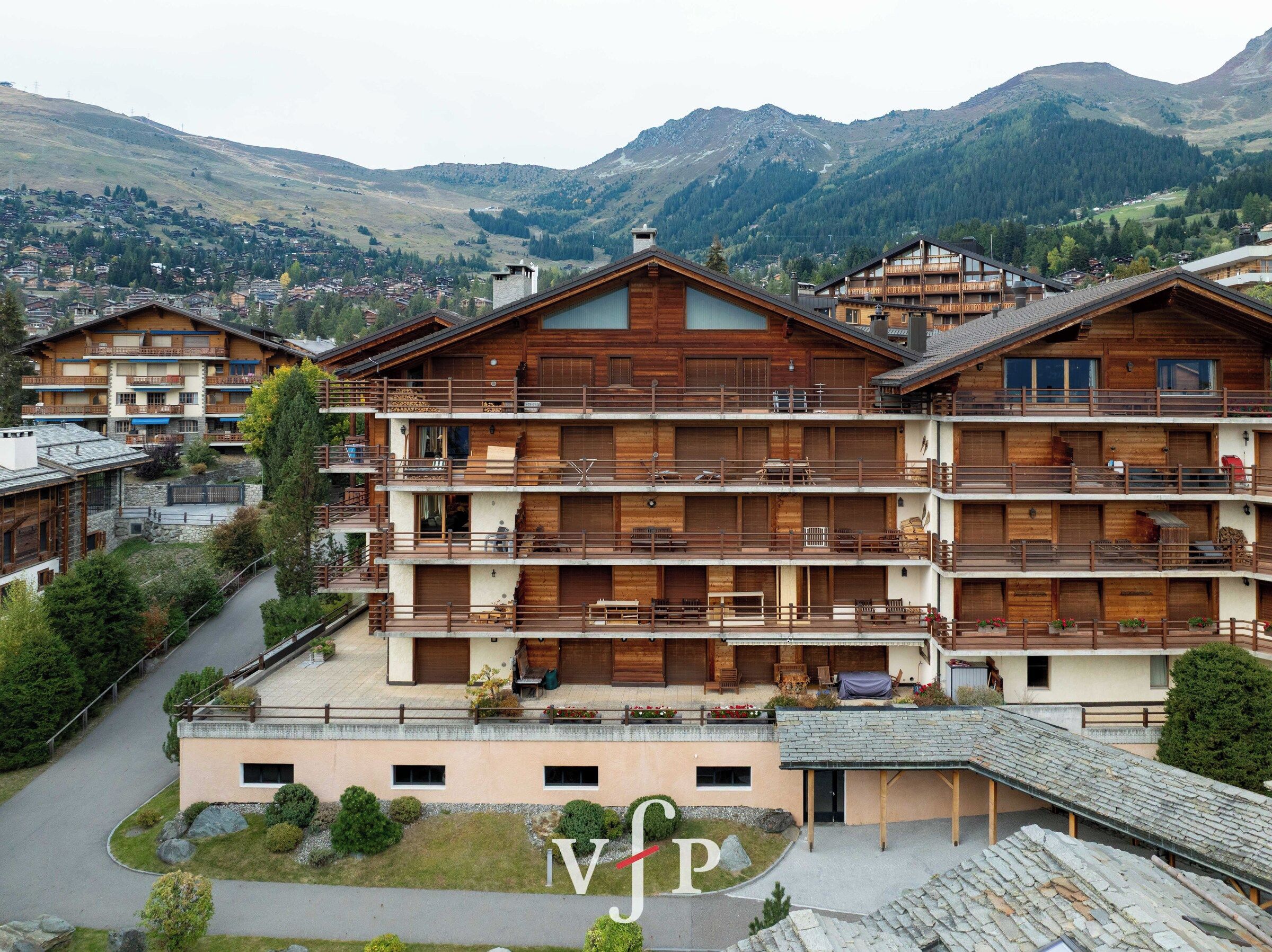 Ein mehrstöckiges Hotel mit Balkonen, im Hintergrund eine Skipiste und eine gebirgige Landschaft.