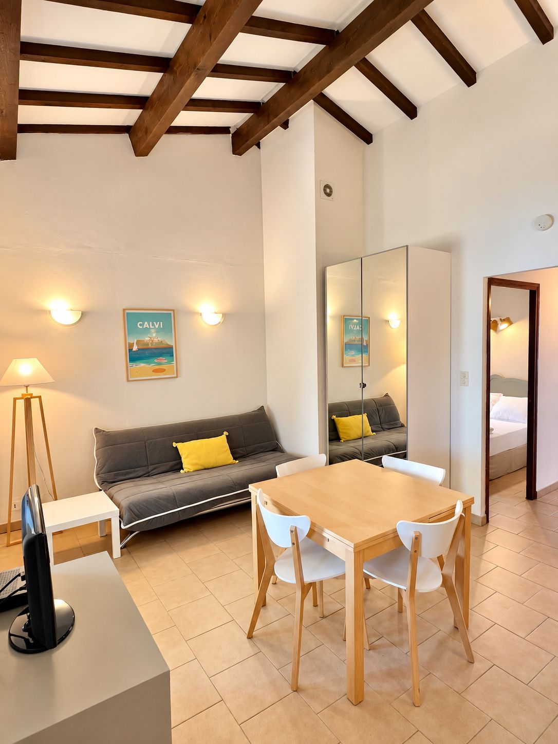 Una habitación moderna con techo de madera, un sofá con cojines amarillos, una mesa de comedor con sillas, un televisor de pantalla plana y un espejo grande.