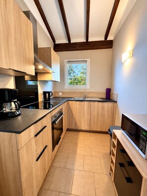 A modern kitchen with wooden cabinets, a built-in oven, a coffee maker, a microwave, and a window with a view of greenery.