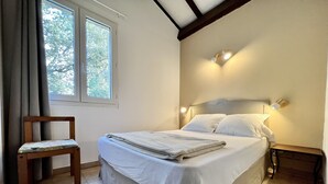 Una cama bien hecha con cabecera, una silla de madera y una ventana con cortinas.
