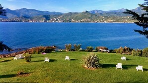 Un espacio verde con sillones blancos y vistas a una gran masa de agua y montañas al fondo.