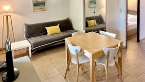 Un espacio habitable compacto con un sofá, una mesa de comedor con sillas, un televisor y una lámpara.