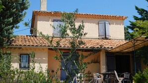 Un edificio de dos plantas con tejado de baldosas, una chimenea y un pequeño balcón con sillas.