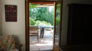 Puerta corredera abierta que da a un patio al aire libre con un banco de madera, una mesa y sillas.