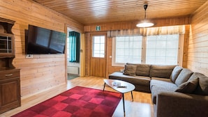 L’intérieur d’un chalet accueillant, avec un plafond en bois, un téléviseur fixé au mur, un canapé, une petite table et un tapis rouge.