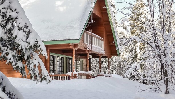 Une cabane en rondins avec un toit à forte pente, un balcon et un paysage enneigé.