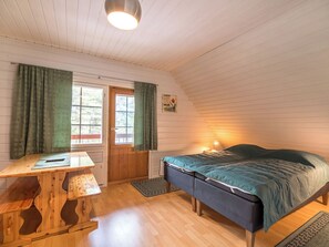 Une pièce avec un bureau en bois, un lit recouvert d’une couverture bleue, une fenêtre avec des rideaux et un luminaire fixé au mur.