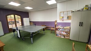 A room with a ping pong table, a bookshelf, a cabinet, and a door with a view of the outside.