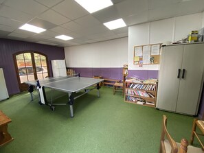 A room with a ping pong table, a bookshelf, a cabinet, and a door with a view of the outside.