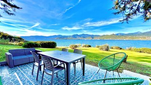 Een terras buiten met een tafel en stoelen, een bank en uitzicht op een meer en bergen.