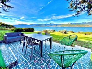 An outdoor patio with a table and chairs, a sofa, and a view of a lake and mountains. - Ground-floor apartment with exceptional views of the ocean, garden, and mountains (Calcatoggio)