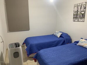 A bedroom with two beds, a window with a blind, a wall-mounted air conditioner, and a poster on the wall. - Departamento excelente en zona top Mza (Mendoza)