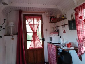 Traditional kitchen with a wooden door, window, and rustic charm, featuring a microwave, kettle, and dishes.