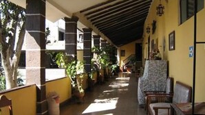 A covered corridor with columns, potted plants, and seating areas. - Hostal Tres Mascaras (Ayacucho)