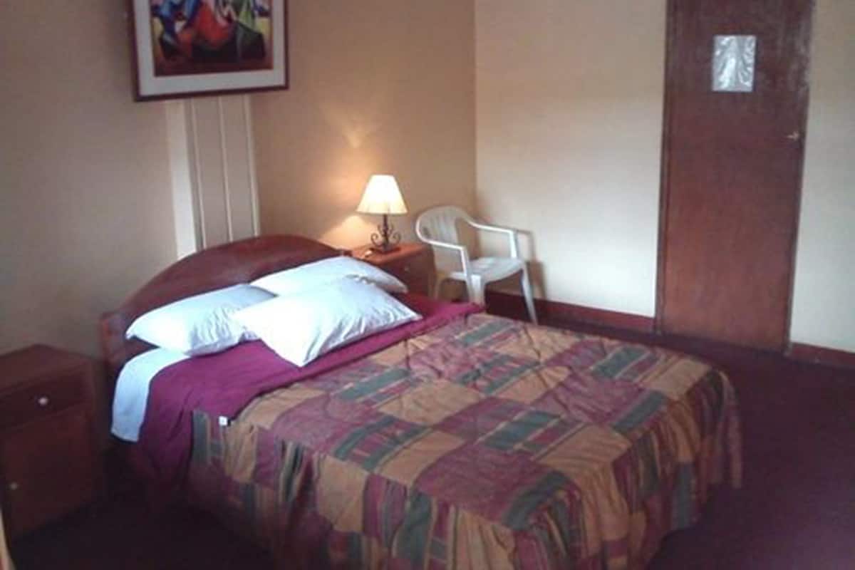 Une chambre d’hôtel avec un lit, une chaise, une table de chevet, une lampe et une porte.