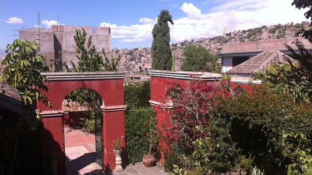 A courtyard with a red archway, potted plants, and a view of a cityscape in the background. - Hostal Tres Mascaras (Ayacucho)