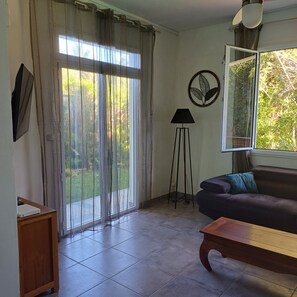 A living room with a sofa, a coffee table, a floor lamp, and a sliding glass door leading to a garden.