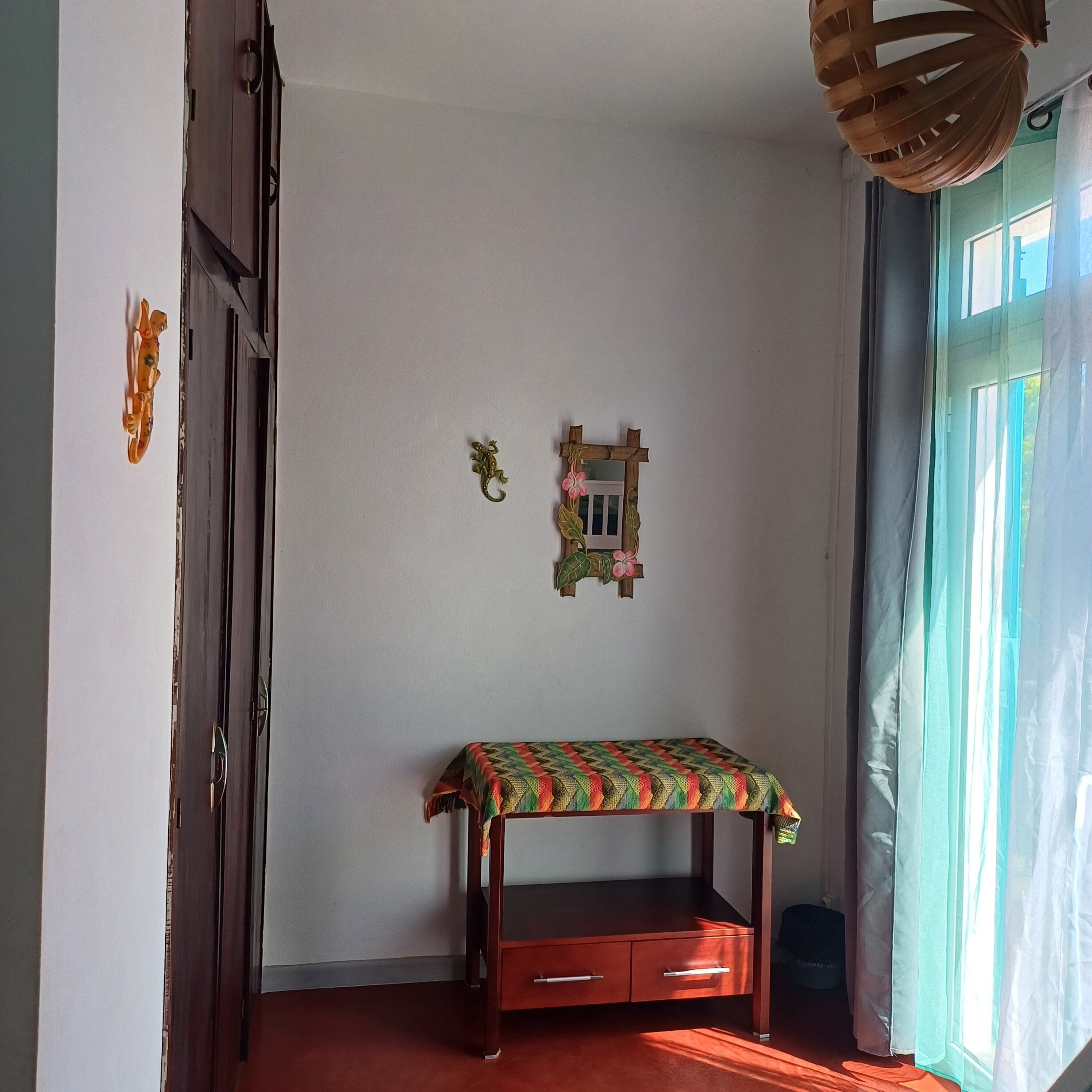 Une pièce avec un banc en bois, un petit objet décoratif fixé au mur et une fenêtre avec des rideaux.
