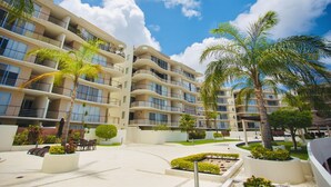 A multi-story hotel with balconies, palm trees, and a landscaped courtyard. - Luxury 2 Bedroom Apartments (Cancun)