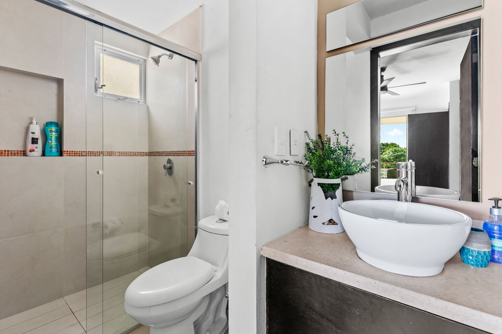 Une salle de bain moderne avec une douche à parois de verre, des toilettes blanches, un grand lavabo blanc et un miroir au-dessus du lavabo.