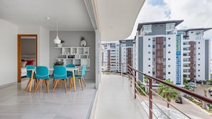 A modern apartment with a balcony, a dining area with blue chairs, and a view of surrounding buildings. - Luxury 2 Bedroom Apartments (Cancun)