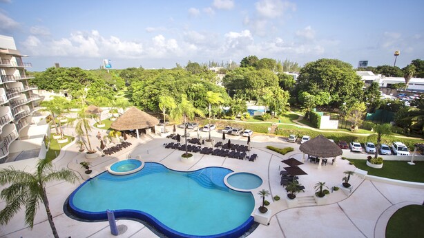 A resort pool area with a large pool, lounge chairs, and umbrellas. - Luxury 2 Bedroom Apartments (Cancun)