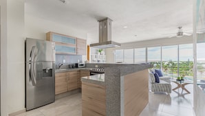 A modern kitchen with a stainless steel refrigerator, wooden cabinets, and a large island. - Luxury 2 Bedroom Apartments (Cancun)