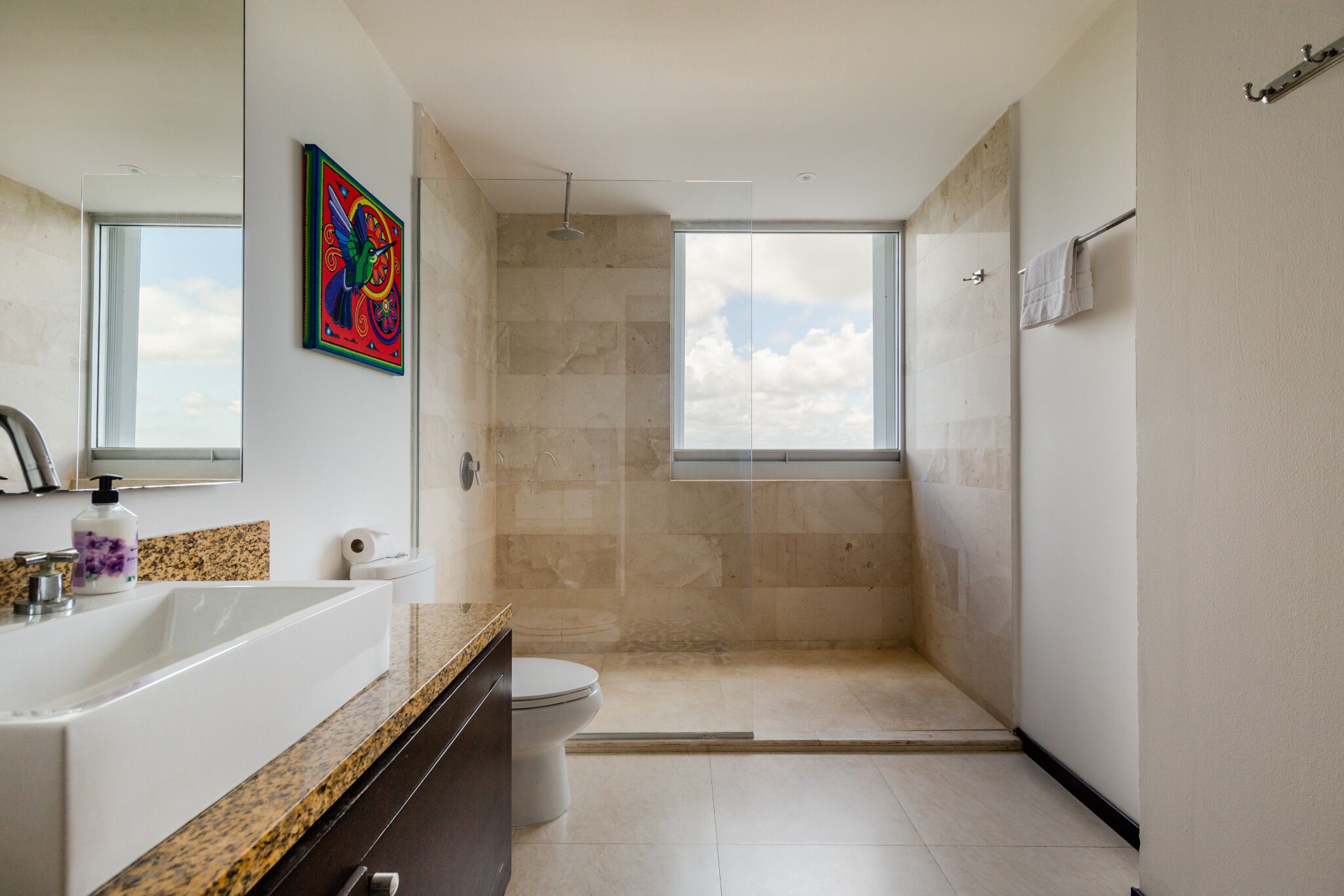 Une salle de bain moderne dotée d’une grande fenêtre, d’une douche et d’un lavabo avec un plan de travail en granit.