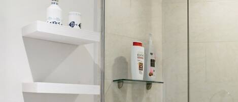 A modern bathroom with a glass shower enclosure, a toilet, and a shelf with toiletries.