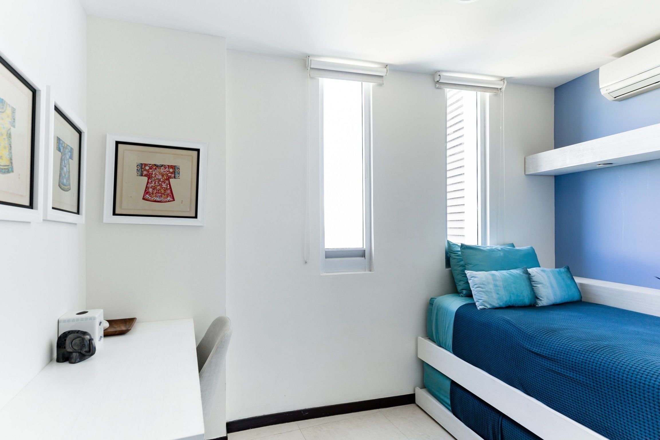 Un dormitorio con cama, escritorio y dos ventanas.