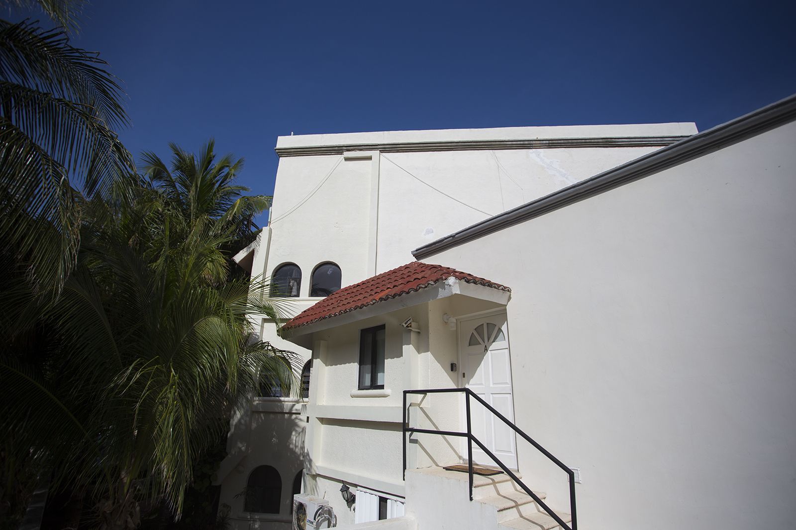 A white building with a red-tiled roof, a staircase, and palm trees.