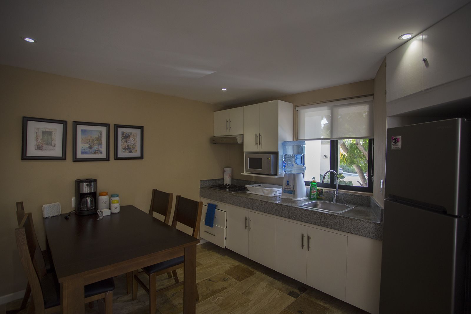 A compact kitchen with white cabinets, a stainless steel refrigerator, a coffee maker, and a water dispenser.