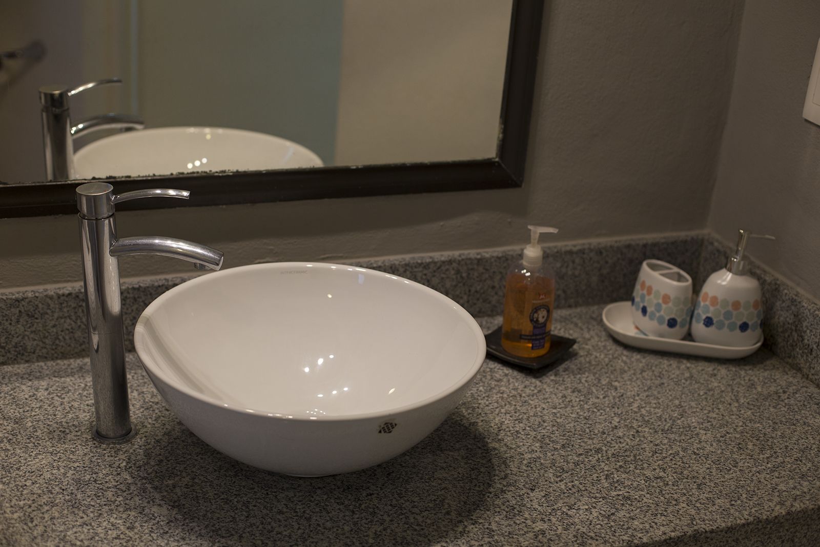 A white sink with a modern faucet, a soap dispenser, and two toiletry cups on a granite countertop.